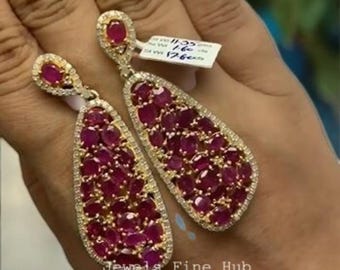 Pode incluir: Um par de brincos pendentes em forma de gota com numerosos rubis de corte oval em vermelho profundo engastados em ouro, rodeados por pequenos diamantes brancos em pavé. Cada brinco tem um rubi no topo e um grupo maior na parte inferior.