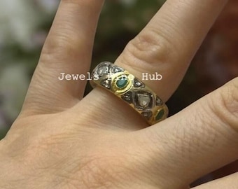 May include: A gold band ring featuring a textured surface with embedded small green gemstones and clear stones in a repeating pattern. The text Jewels Fine Hub is visible across the centre of the ring. The band has a wide profile and a metallic finish.
