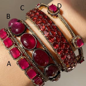 Op de afbeelding: Een collectie van armbanden met robijnen en diamanten. De armbanden hebben verschillende ontwerpen, waaronder rechthoekige en ovale robijnen, en een armband met een getextureerd robijn oppervlak. De armbanden zijn gezet in zilver- of goudkleurig metaal. De afbeelding bevat de tekst "Jewels Fine Hub".