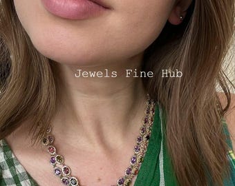 May include: A multi-colored gemstone necklace with the text "Jewels Fine Hub". The necklace features a double strand design with a variety of colorful gemstones set in a gold-toned metal. The gemstones include shades of purple, green, yellow, and red.