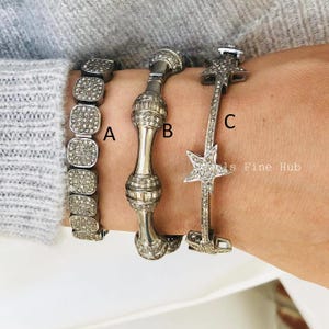 Op de afbeelding: Drie zilveren armbanden met sprankelende versieringen. Armband A is een vierkant schakelontwerp. Armband B heeft een cilindrische vorm met decoratieve uiteinden. Armband C heeft een sterontwerp.