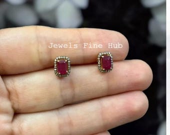 Pode incluir: Um par de brincos de tarracha com rubis vermelhos retangulares rodeados por pequenas pedras brancas numa cravação metálica. O texto Jewels Fine Hub é visível acima dos brincos. Estes brincos têm uma forma retangular clássica com uma pedra central vermelha vibrante e uma borda cintilante, proporcionando uma visão clara do design da joalharia.