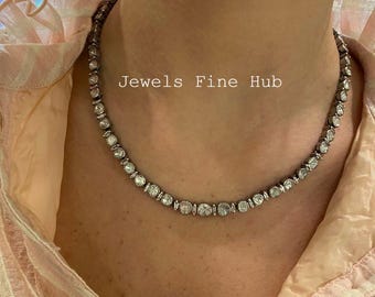 Puede incluir: Un collar plateado con numerosas piedras preciosas redondas y transparentes. El collar se lleva alrededor del cuello y se coloca sobre una camisa rosa claro. El texto "Jewels Fine Hub" es visible.
