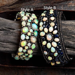 May include: Two ornate bracelets, labeled Style A and Style B, are displayed. Style A features numerous opals and small diamonds. Style B showcases opals and dark blue stones, with a black band and small diamonds. The bracelets are set against a dark wood background.