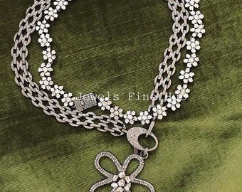 Puede incluir: Un collar plateado con un colgante de flor. El collar tiene dos cadenas, una con un diseño floral y otra con un diseño de eslabones. El colgante de flor es plateado y tiene un diseño de diamantes. El texto "Jewels Fine" es visible.