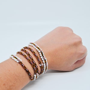 Op de afbeelding: Een meerlaags armband met witte kralen en rode, gele en zwarte geweven draden.