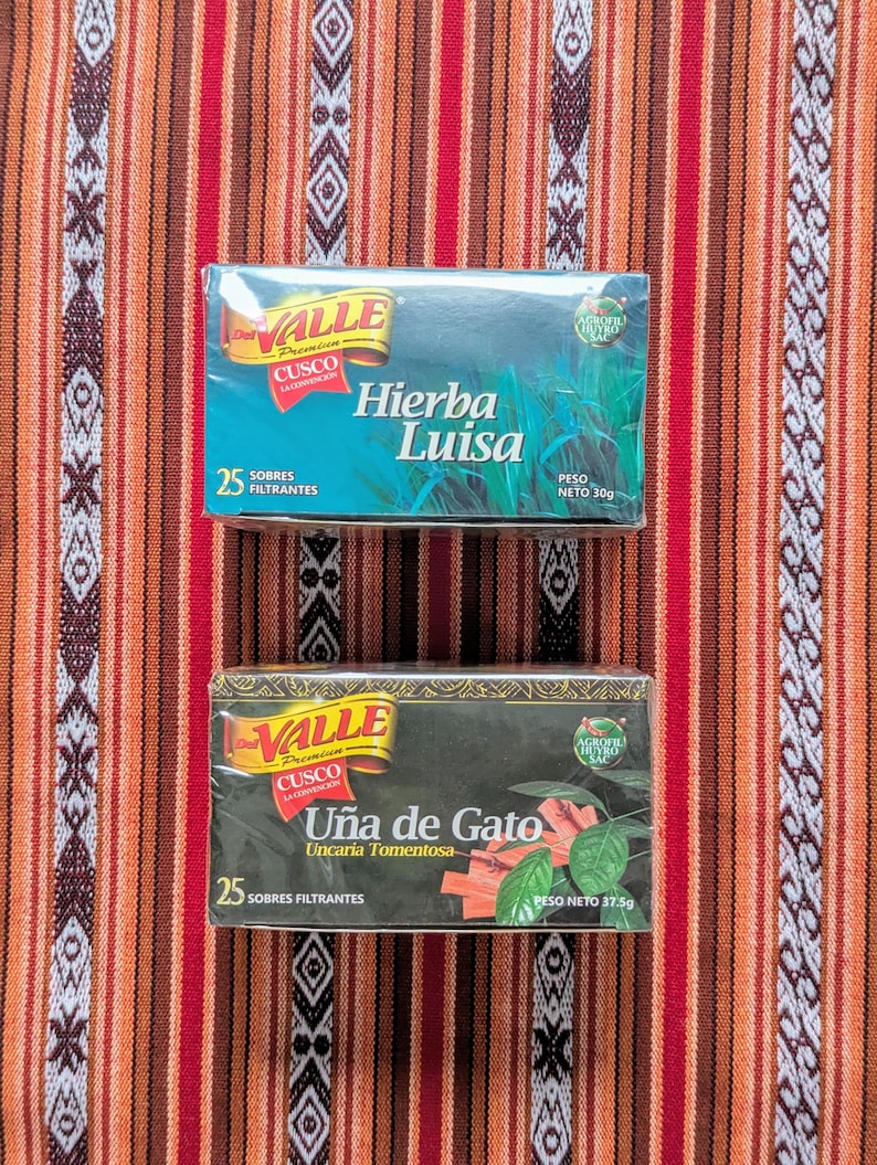 May include: Two boxes of herbal tea bags. The top box is blue and green and says "Hierba Luisa" with a picture of the herb. The bottom box is black and green and says "U&ntilde;a de Gato" with a picture of the herb.