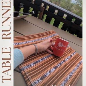May include: Brown and orange striped table runner with white and blue geometric patterns. A red mug with the word "Perú" is held over the runner. The text "TABLE RUNNERS" and "Déco Inca" are also visible.
