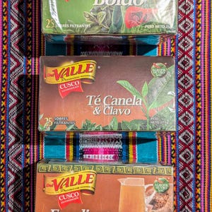 May include: Three boxes of Valle Premium Cusco tea bags. The boxes are brown with gold accents and feature images of the tea ingredients. The top box is labeled "Boldo" and features a green leaf with a red flower. The middle box is labeled "T&eacute; Canela & Clavo" and features a cinnamon stick and cloves. The bottom box is labeled "Emoliente" and features a brown pitcher with a yellow liquid and a bundle of herbs.