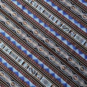 Pode incluir: Um close-up de um tecido com um padrão repetitivo de listras diagonais em tons de marrom, azul e branco. O padrão apresenta formas e desenhos geométricos.