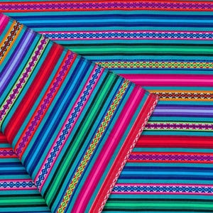 Op de afbeelding: Een stof met een levendig, meerkleurig streeppatroon met horizontale banden in felblauw, groen, rood, paars en roze. Het ontwerp bevat ingewikkelde, herhalende geometrische motieven die tussen de effen gekleurde strepen zijn geplaatst.