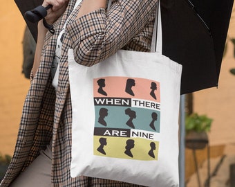 May include: A person wearing a plaid coat and glasses is holding a black umbrella and a white tote bag with the text "WHEN THERE ARE NINE" and nine silhouettes of people in different colours.