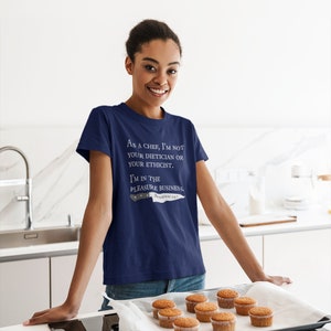 May include: A navy blue t-shirt with white text that reads "As a chef, I'm not your dietician or your ethicist. I'm in the pleasure business. Boudain 24/7". A knife graphic is below the text.