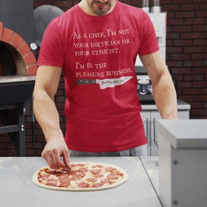 May include: A red t-shirt with the text "As a chef, I'm not your dietician or your ethicist. I'm in the pleasure business. Bourdain 24/7" and a knife graphic. A person is placing pepperoni on a pizza.