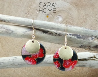 May include: A pair of gold earrings with a black and red floral design. The earrings are made of metal and have a round shape. The floral design is intricate and features red flowers with white accents.