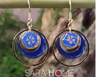 May include: Gold earrings with a blue and gold patterned circle design. The earrings have a double circle design with a smaller circle inside a larger circle.