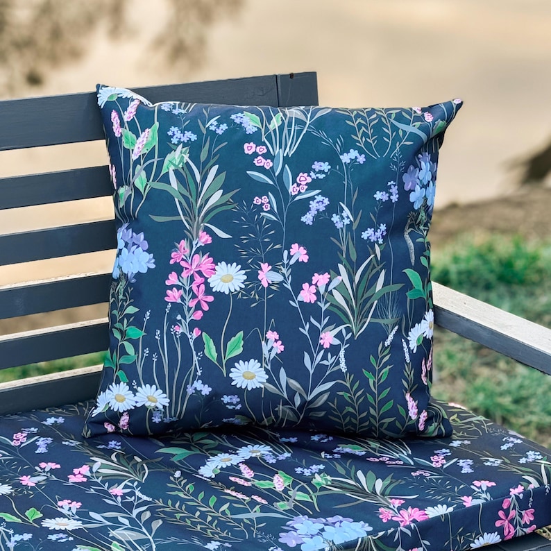 May include: A dark blue throw pillow with a floral pattern featuring pink, white, and blue flowers on a dark blue background. The pillow is sitting on a matching dark blue cushion with a similar floral pattern.