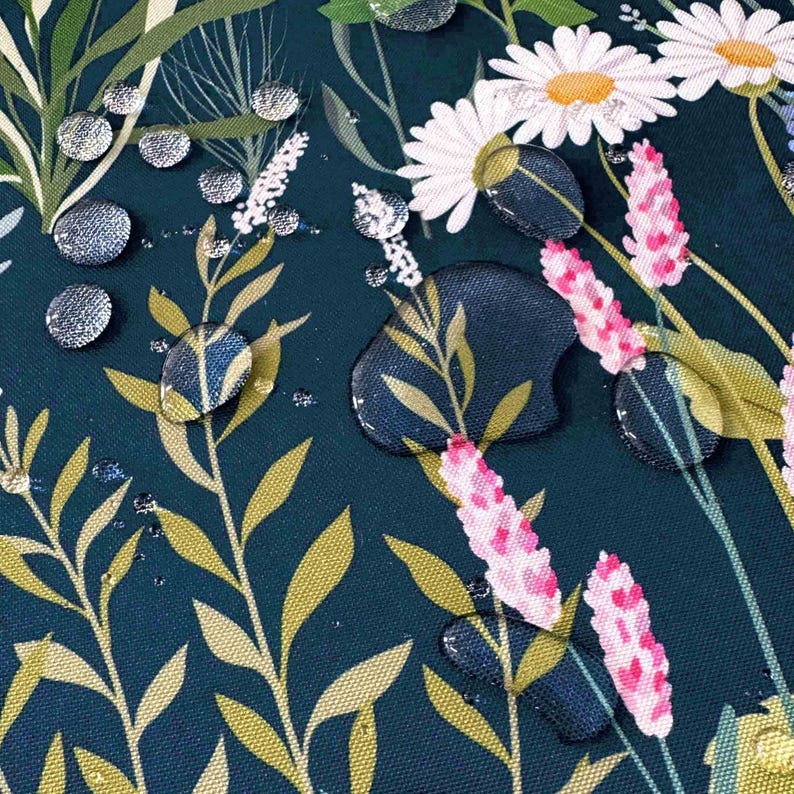 May include: Water droplets on a dark blue fabric with a floral pattern. The pattern features white daisies, pink flowers, and green leaves.