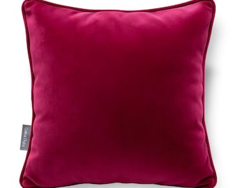 May include: A square, deep magenta velvet throw pillow with piped edges. The fabric has a soft, plush texture. A small, grey rectangular fabric tag on the left side features the white text Celina Digby printed in a clear, sans-serif font.