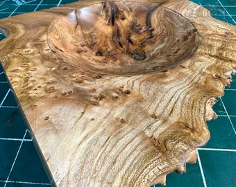 Könnte beinhalten: Eine Holzschale mit natürlicher Holzoptik und einem einzigartigen Maserungsmuster. Die Schale ist aus einem einzigen Stück Holz gefertigt und hat eine tiefe, abgerundete Form.