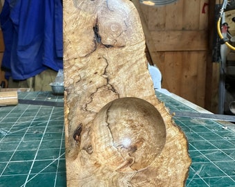 May include: A wooden bowl with a natural wood finish and a round, smooth interior. The bowl is made from a single piece of wood with a unique grain pattern.
