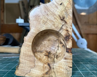 May include: A wooden bowl with a natural wood finish and a unique, irregular shape. The bowl has a large, round indentation in the center.