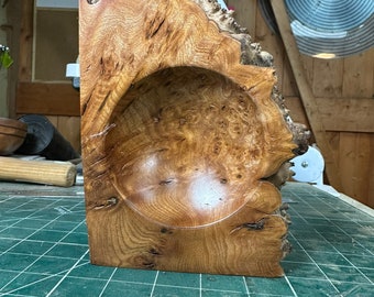 Könnte beinhalten: Eine Holzschale mit einer natürlichen braunen Oberfläche. Die Schale ist aus einem einzigen Stück Holz gefertigt und hat eine einzigartige, organische Form. Die Schale steht auf einer grünen Schneidematte.