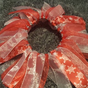 May include: A red and white ribbon hair bow with a snowflake pattern. The bow is made of multiple layers of ribbon and is tied together in the center.