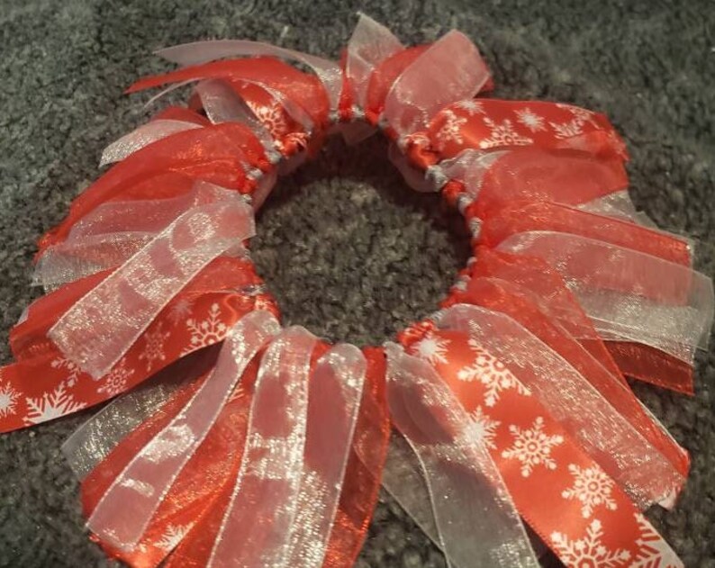 May include: A red and white ribbon hair bow with a snowflake pattern. The bow is made of multiple layers of ribbon and is tied together in the center.