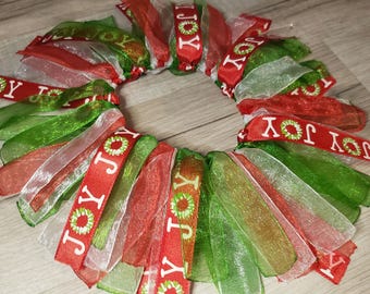Könnte beinhalten: Ein Weihnachtskranz aus rotem, grünem und weißem durchsichtigem Band mit dem Wort "JOY" auf jedem Band.