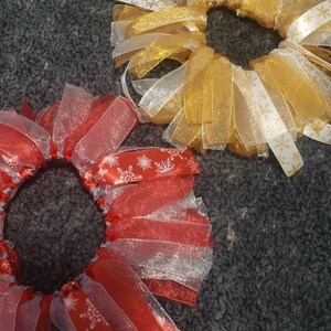 May include: Two Christmas-themed hair scrunchies. One is red with white snowflakes and the other is gold with white snowflakes.