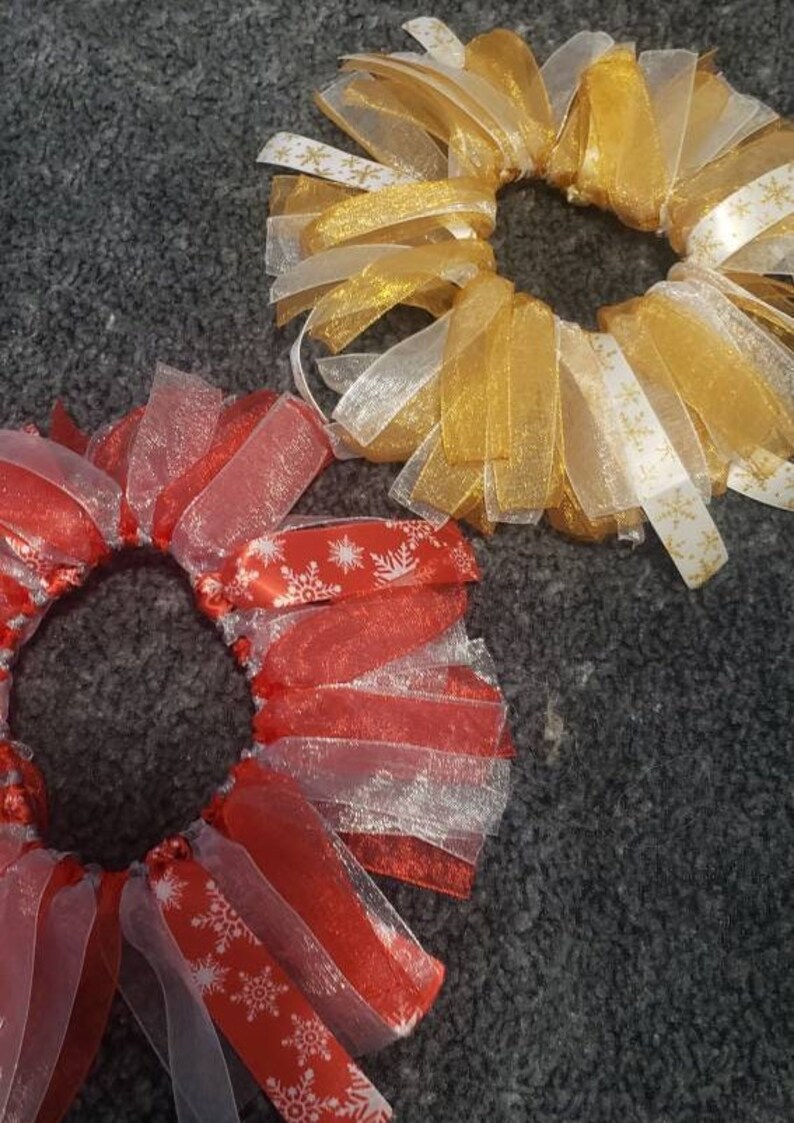 May include: Two Christmas-themed hair scrunchies. One is red with white snowflakes and the other is gold with white snowflakes.
