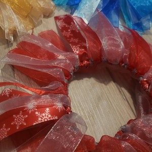 May include: A red and white ribbon wreath with snowflake patterns. The wreath is made of multiple layers of sheer ribbon and is tied together with a white ribbon.