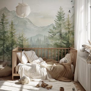 May include: A nursery with a wooden crib, soft bedding, and a forest-themed mural. The crib is filled with white pillows, a cream-colored blanket, and a brown throw. Wooden toy cars are on the rug. A paper lantern hangs from the ceiling.