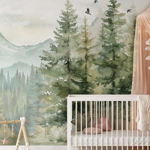 May include: A nursery with a forest-themed mural featuring watercolor trees, mountains, and flying birds. A white crib with a white mattress, pillows, and a blanket is in the foreground. A wooden baby gym and a pink canopy add to the decor.