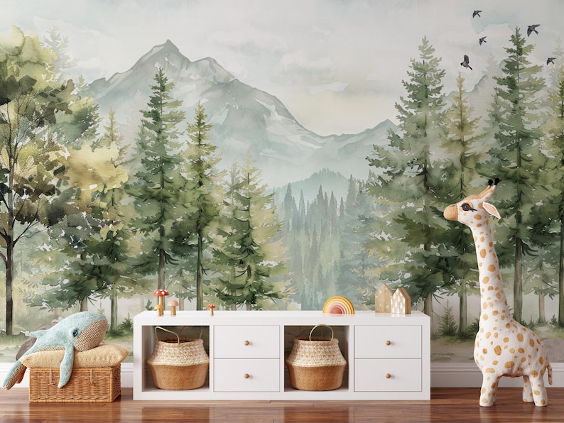 May include: A whimsical nursery scene featuring a mountain and forest mural. A white cabinet holds woven baskets and decorative items. A plush giraffe and whale add playful elements to the room. The color palette includes greens, browns, and whites.
