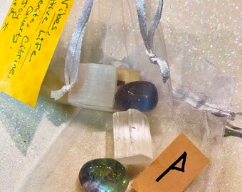 May include: A white organza bag filled with crystals and a small card with the rune "A" written on it. The bag is labeled "Positive Vibes" and includes a list of crystals: Selenite, Citrine, Aqua Aura Quartz, and a Rune of Joy. The bag also includes a Reiki Charge.