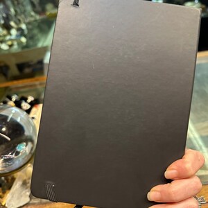 Op de afbeelding: Zwart hardback journal met een zwarte elastische band sluiting en een zwart lint bladwijzer.