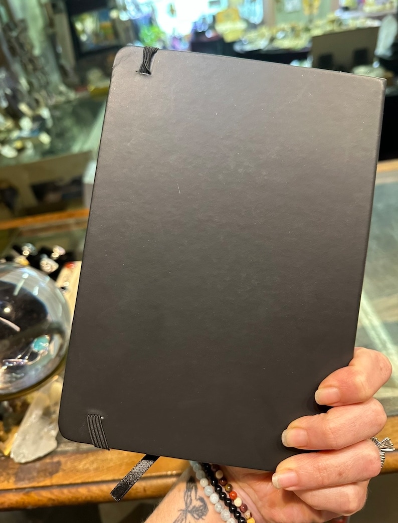 Op de afbeelding: Zwart hardback journal met een zwarte elastische band sluiting en een zwart lint bladwijzer.