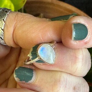 May include: A silver ring with a teardrop-shaped moonstone. The stone has a rainbow sheen and is set in a simple band.