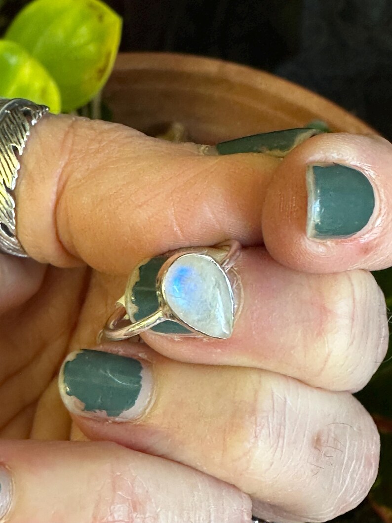 May include: A silver ring with a teardrop-shaped moonstone. The stone has a rainbow sheen and is set in a simple band.