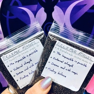 May include: Two small clear plastic bags filled with dark brown incense. The bags have white labels with the text "ECLIPSE MAGIC" and a list of benefits: "The impossible is possible", "Internal strength", "Dream and wish magic", and "Finding balance".