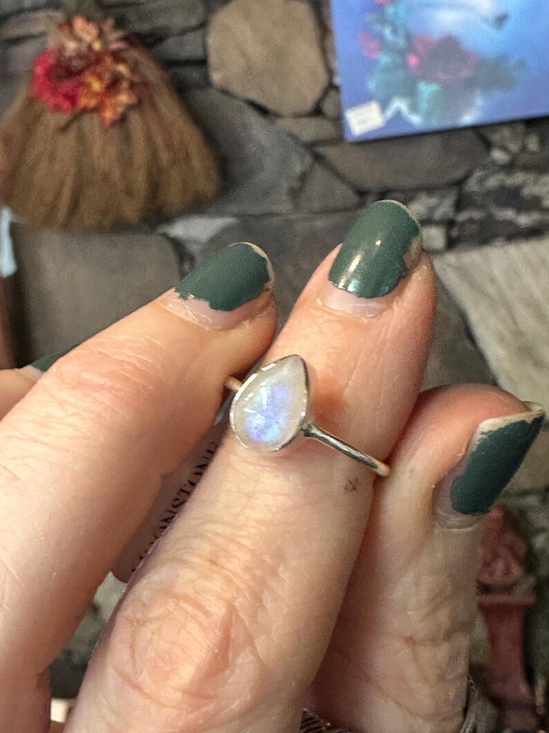 May include: A silver ring with a teardrop-shaped moonstone. The stone is iridescent and has a milky white color.