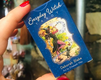 May include: A blue and white box with the text "Everyday Witch Tarot Mini" and "Deborah Blake Art by Elisabeth Alba". The box features an illustration of a witch with a cat.