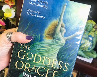 May include: A blue and green box with the text "The Goddess Oracle Deck & Book Set" on the front. The box features an illustration of a woman with long flowing hair, reaching up towards a bright sky.