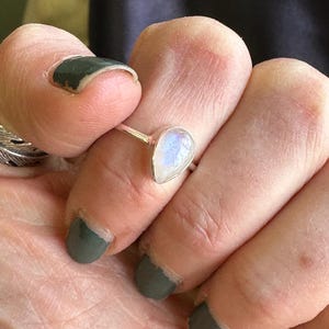 May include: A silver ring with a teardrop-shaped moonstone. The stone is iridescent and has a milky white color.