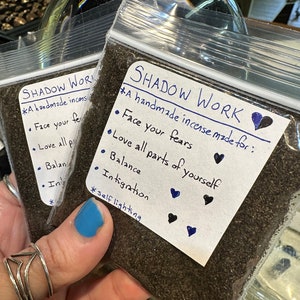 May include: A small bag of loose incense labeled "Shadow Work" with the text "A handmade incense made for: Face your fears, Love all parts of yourself, Balance, Integration, *self lighting" and four small black hearts.