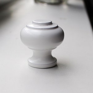 May include: White ceramic cabinet knob with a rounded top and a smooth, polished finish.