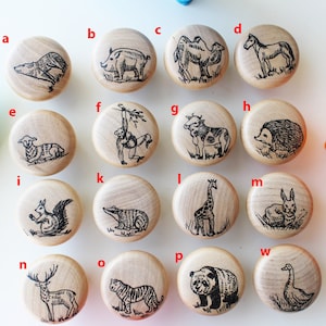 May include: Set of 16 wooden knobs with animal illustrations. The knobs are round and have a natural wood finish. The animals include a deer, a tiger, a panda, a goose, a rabbit, a hedgehog, a cow, a monkey, a squirrel, a badger, a giraffe, a camel, a horse, a pig, a sheep, and a wolf.