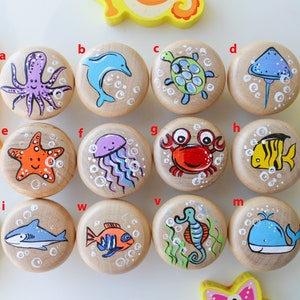 Puede incluir: Un conjunto de 12 pomos de madera con diseños de animales marinos pintados. Los pomos presentan una variedad de criaturas marinas, incluyendo un delfín, un pulpo, una estrella de mar, una medusa, un cangrejo, un pez, un tiburón, un caballito de mar y una ballena. Los pomos están pintados en colores brillantes y son perfectos para agregar un toque de fantasía a cualquier habitación.
